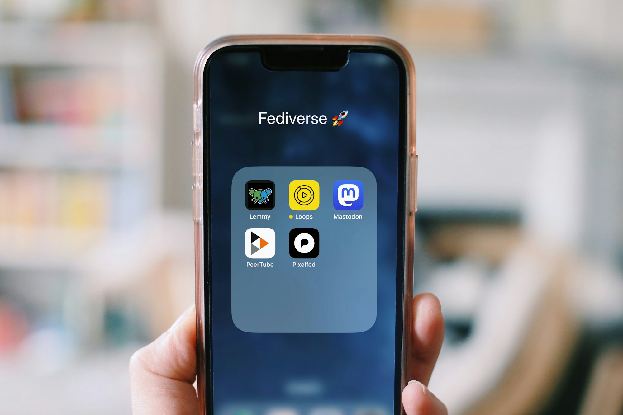 Photograph of a hand holding a smartphone. The phone has a folder open called "Fediverse". Inside the folder are icons for the Lemmy, Loops, Mastodon, PeerTube, and Pixelfed apps. fediverse.jpg